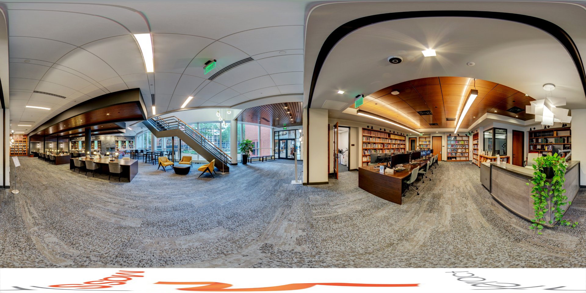 A panoramic view of a modern library with a large open area, featuring study tables, bookshelves, and a staircase leading to an upper level. The space includes comfortable seating, workstations with computers, and a reception desk. The design incorporates wood paneling, soft lighting, and expansive windows.